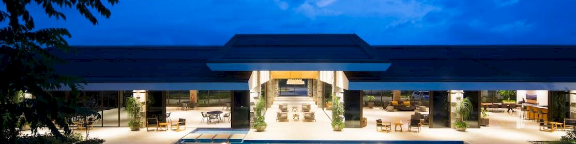 A luxurious pool reflecting lights at night, with a modern building in the background under a deep blue sky.