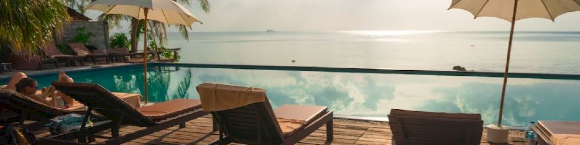 A serene poolside scene with lounge chairs, umbrellas, and a scenic view of the ocean at sunset.