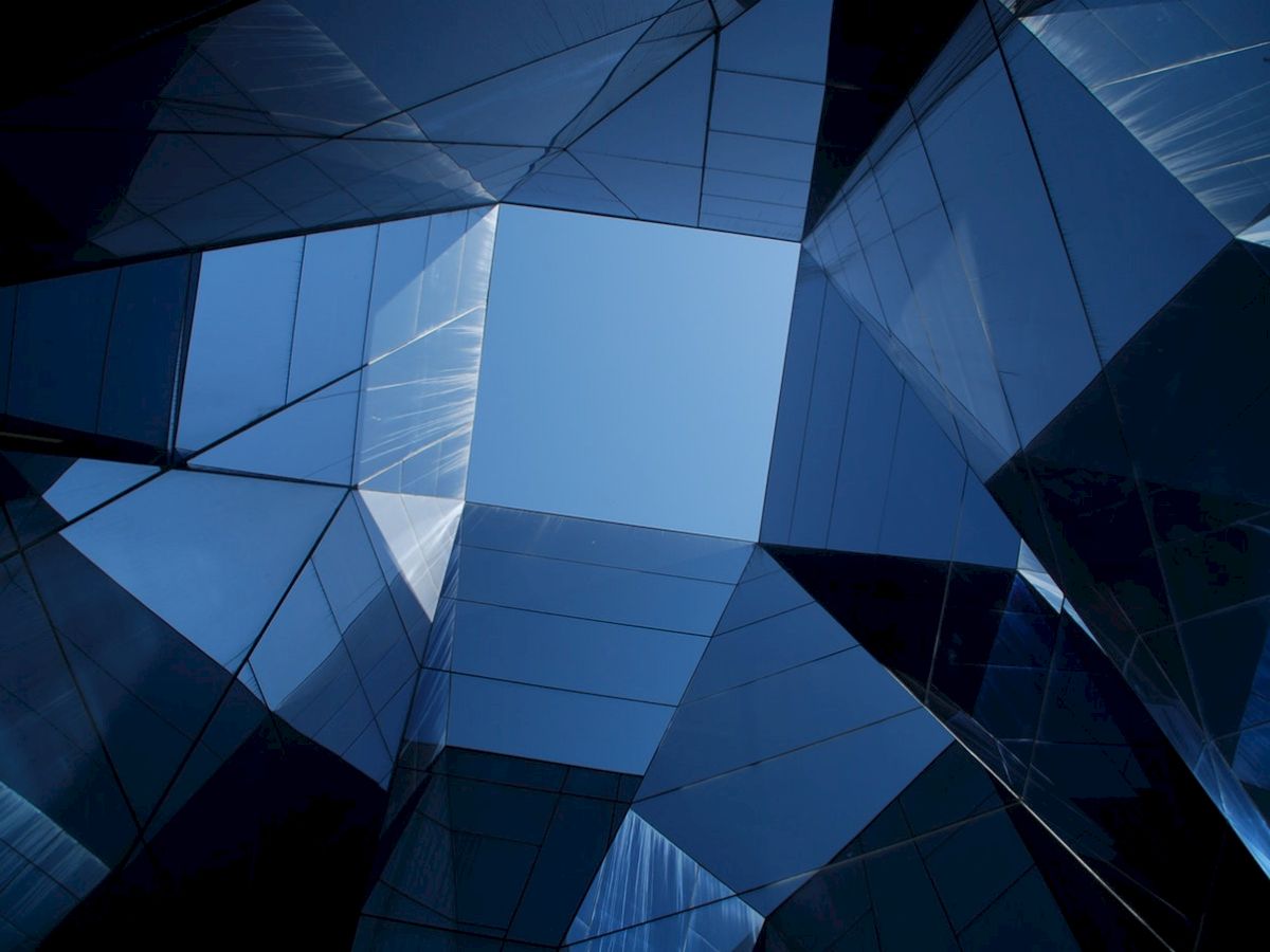 The image shows a geometric view looking up at reflective blue glass buildings, creating a sense of symmetry and modern architecture.