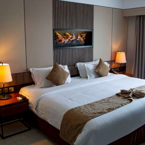 A hotel room with a large bed, two bedside tables with lamps, and a decorative wall feature. Curtains cover a window.