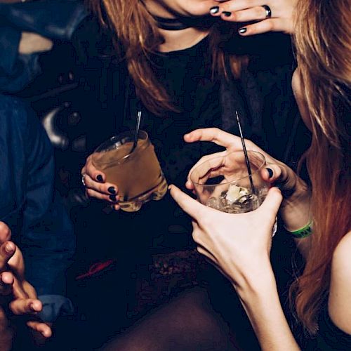 People are enjoying a social gathering, holding drinks with straws, and laughing together in a lively setting.