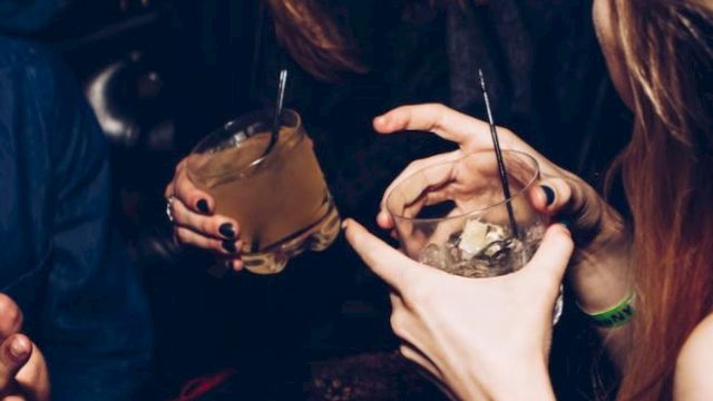 People are enjoying a social gathering, holding drinks with straws, and laughing together in a lively setting.