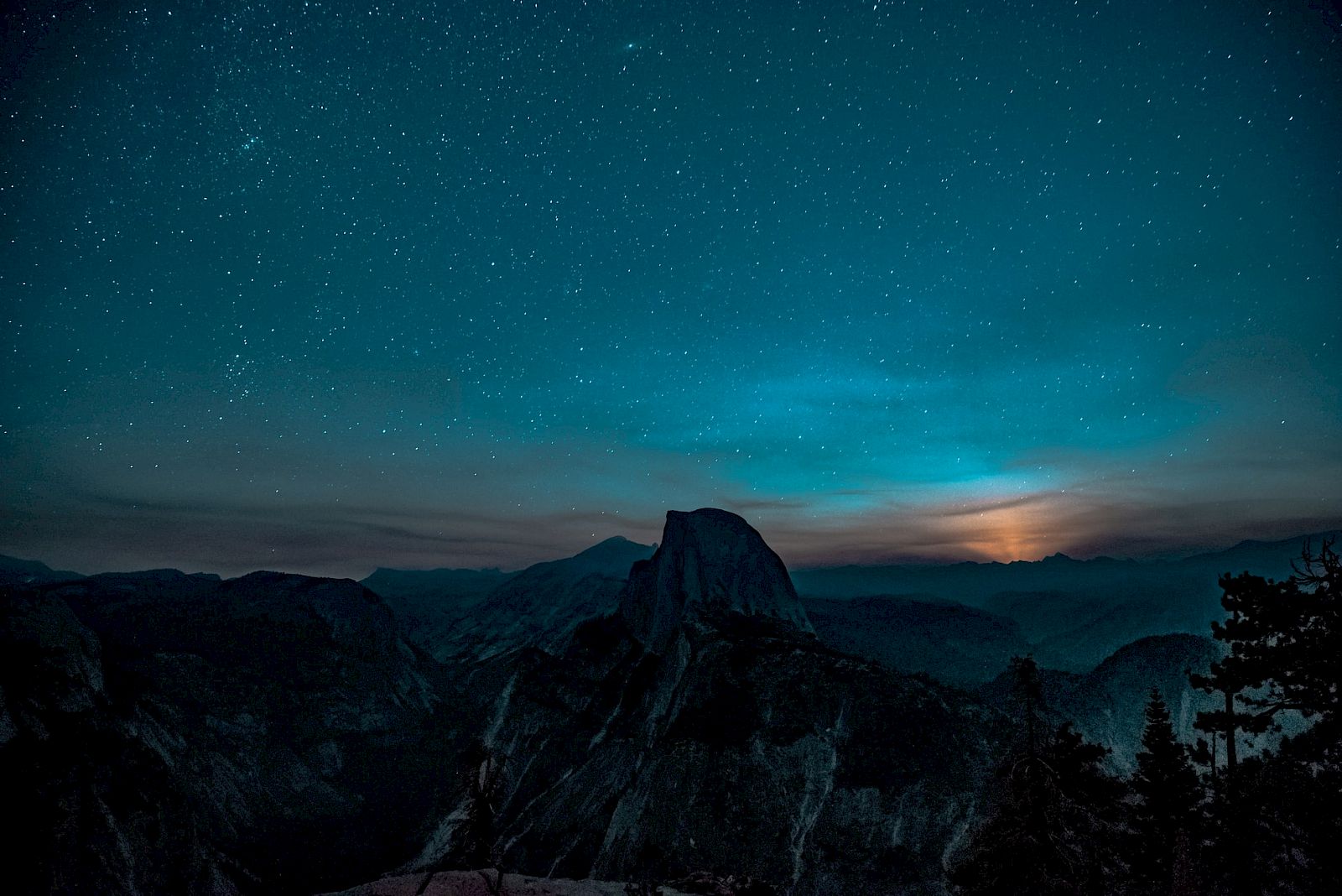 A starry night sky over a mountain landscape with a glowing moon or sun on the horizon.