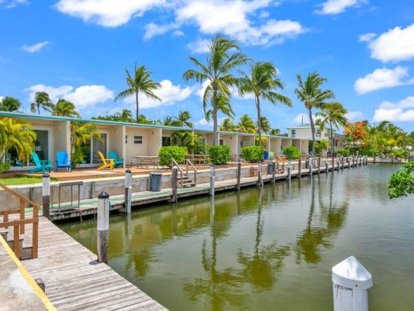 A scenic waterfront view with tropical-style houses, palm trees, and a clear blue sky reflected in the calm waterway.