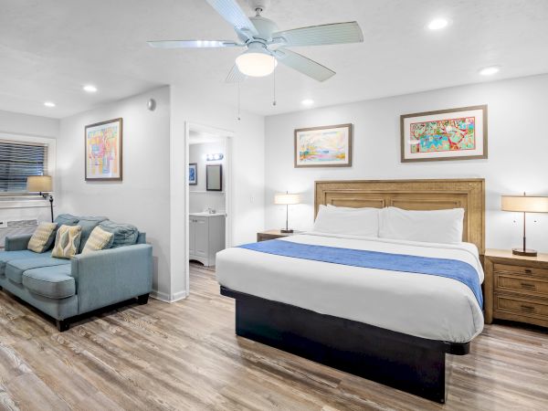 A well-lit hotel room with a bed, blue sofa, wall art, and wooden flooring, creating a cozy atmosphere.