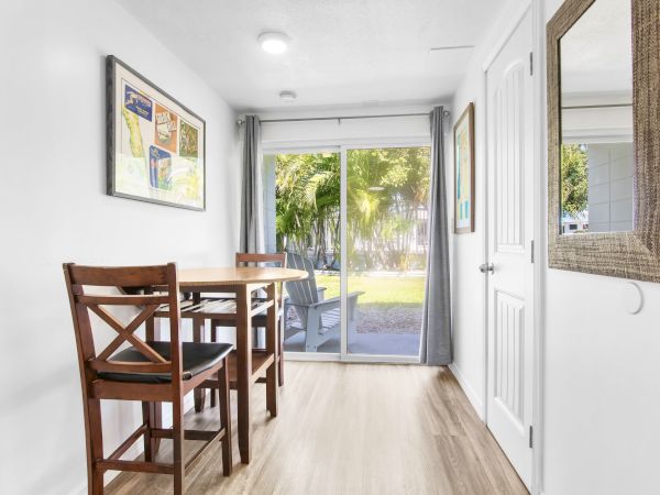A small dining area features a wooden table with two chairs, artwork on the walls, and a sliding glass door leading outside.