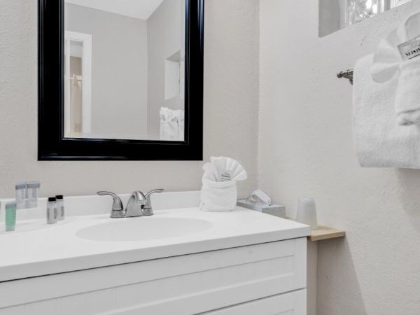 A clean bathroom with a white vanity, a mirror, towels, and toiletries neatly arranged on the countertop and a towel rack.