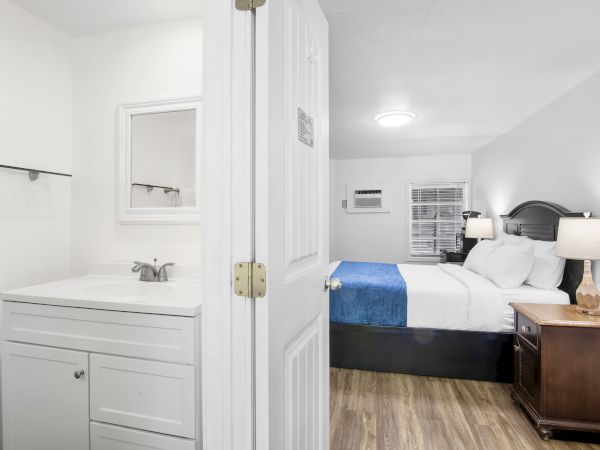 A hotel room with a bed, nightstand, lamps, and a small sink area is visible near the entrance.