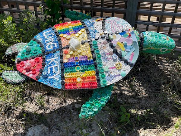 A turtle sculpture made from colorful recycled materials and bottle caps, lying on the ground.