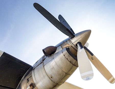The image shows a close-up of a propeller on an aircraft, with four blades against a clear sky background.