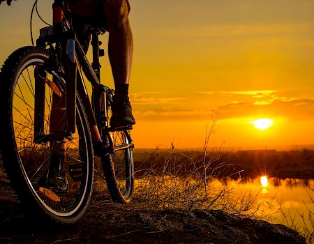 A person on a bicycle is silhouetted against a vibrant sunset, overlooking a reflective body of water, with a scenic horizon view.
