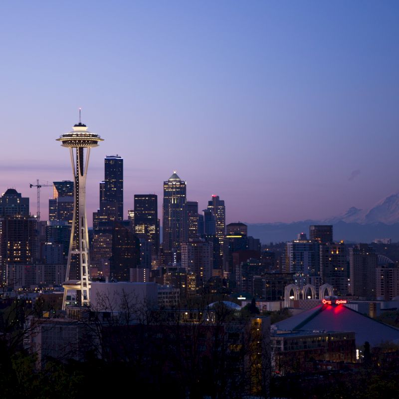 A cityscape view at dusk shows a skyline with a prominent tower, illuminated buildings, and a mountain in the background.
