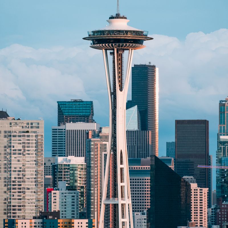 The image features the Space Needle against a city skyline with modern skyscrapers and a cloudy sky in the background.