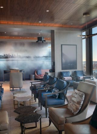 A modern lounge with leather chairs, large windows offering a scenic view, and a wall mural of a city skyline.