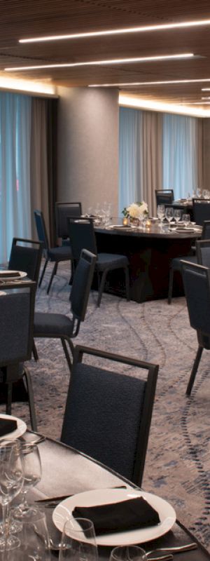 The image shows an elegant banquet room with round tables set for dining, featuring black chairs and dim lighting.