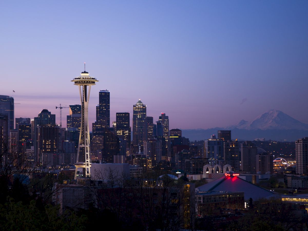 The image shows a cityscape at dusk with a prominent observation tower, skyscrapers, and a mountain in the background under a twilight sky.